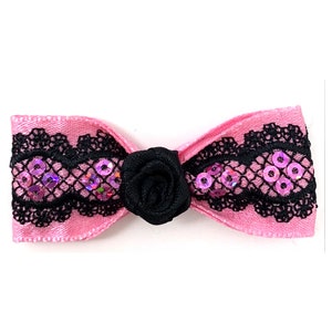 May include: A pink satin bow with black lace trim and pink sequins. A black fabric rose is in the centre of the bow.
