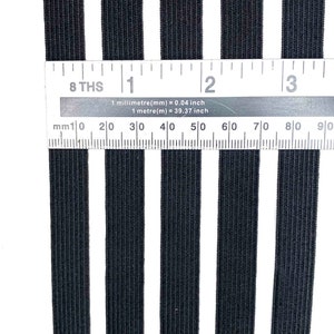 May include: Five black elastic bands, each approximately 1 inch wide, are laid out next to a ruler. The ruler measures in inches and millimeters. The elastic bands are all the same size and are made of a stretchy material.
