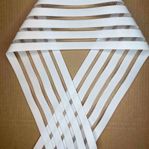 May include: White elastic trim with thin, translucent brown stripes. The trim is folded in half and the stripes are visible on both sides.