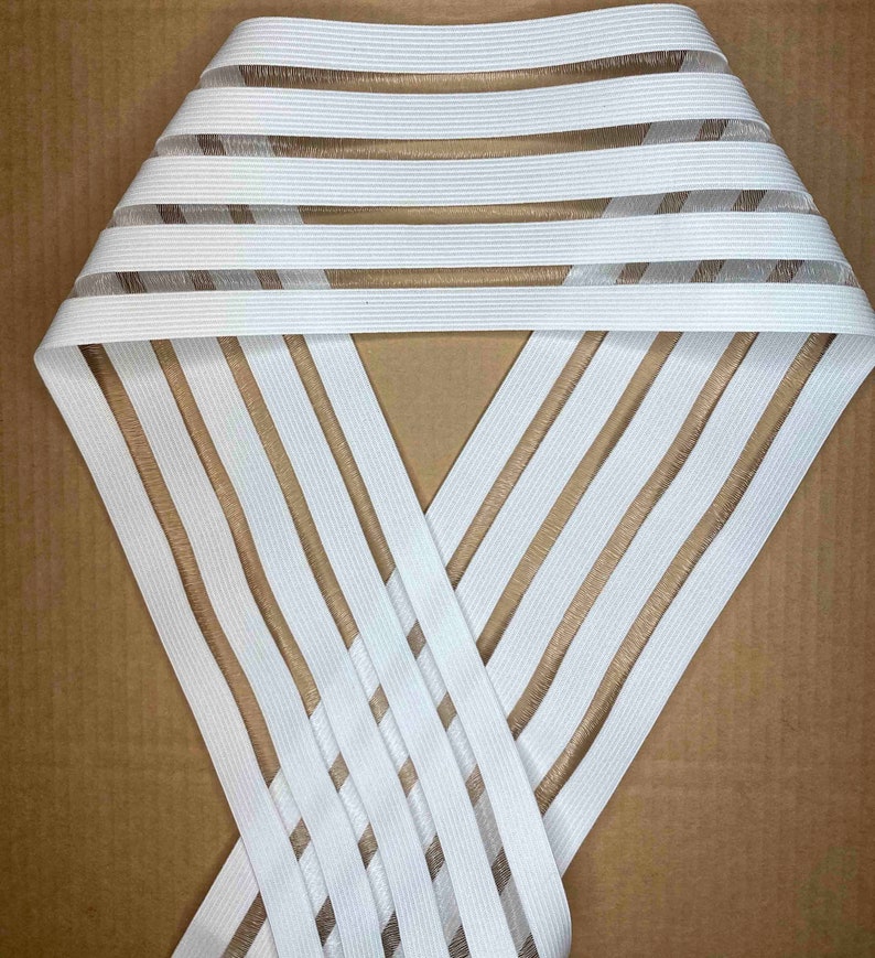 May include: White elastic trim with thin, translucent brown stripes. The trim is folded in half and the stripes are visible on both sides.