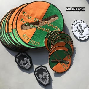 Può includere: Un set di 12 toppe ricamate con un designo verde e arancione con il testo "C.V. De Foute Frikandell" e "EST. 2023". Ci sono anche due toppe più piccole con teschio bianco e nero.