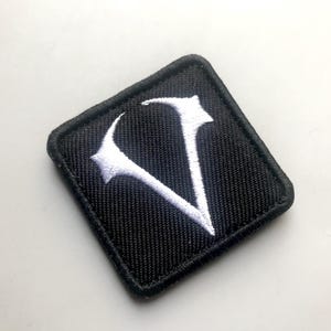 May include: A black fabric patch with a white embroidered letter V.