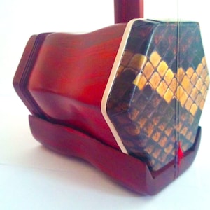 Puede incluir: Un erhu chino de madera roja con una caja de resonancia con estampado de piel de serpiente.