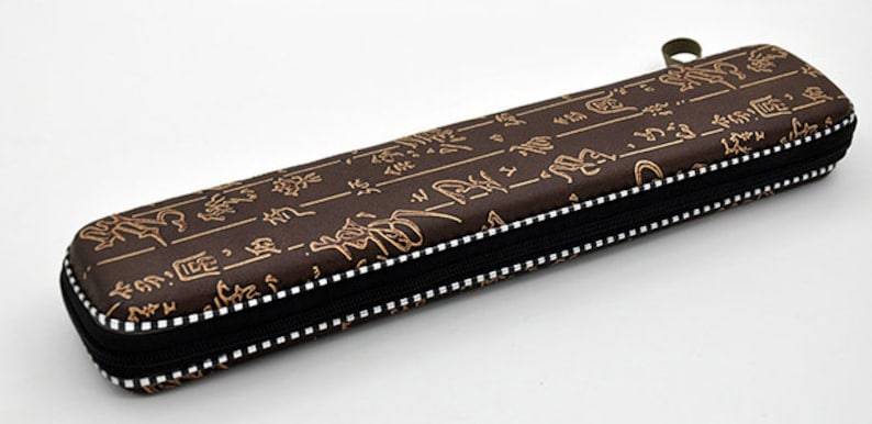 Puede incluir: Una funda marr&oacute;n con cremallera, cremallera negra y costuras blancas. La funda est&aacute; cubierta con un patr&oacute;n de caracteres chinos dorados.