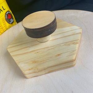 May include: A wooden hexagonal base with a round wooden knob on top. The knob has a dark brown ring around the top.