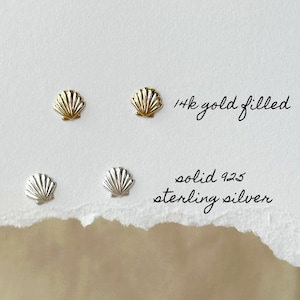 May include: Two pairs of small seashell-shaped stud earrings. The top pair is gold-colored with the text 14k gold filled next to it. The bottom pair is silver-colored with the text solid 925 sterling silver written next to it.