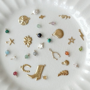 May include: A collection of gold-toned charms and beads, including a horseshoe, a cowboy boot, a star, a seashell, a feather, a lightning bolt, a four-leaf clover, a starfish, a cross, a sand dollar, a seahorse, and various colored beads.