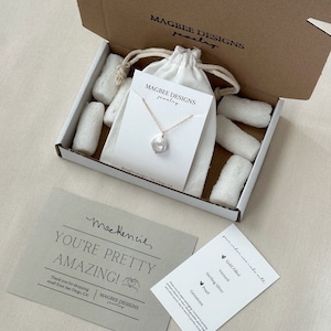 May include: A gold chain necklace with a single white baroque pearl pendant on a display card inside a cardboard box with white packing peanuts and a drawstring pouch. Includes a thank you note and a card listing materials like gold filled.