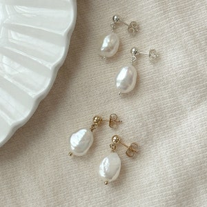 May include: Two pairs of drop earrings featuring irregular white freshwater pearls. One pair is set on silver-tone metal posts with butterfly backs, and the other pair is set on gold-tone metal posts with matching butterfly backs.