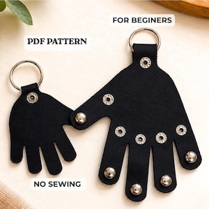 May include: Two black hand-shaped leather keychains with silver metal snap buttons and silver key rings. The text on the image reads PDF PATTERN, FOR BEGINNERS, and NO SEWING. The smaller hand is attached to the larger hand by a silver snap button.