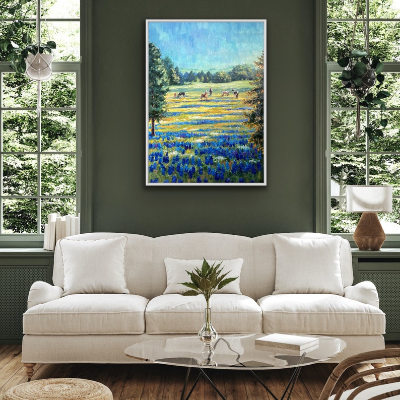 May include: A framed landscape painting featuring a vibrant field of bluebonnets in the foreground, transitioning into a grassy meadow with several horses grazing under a bright blue sky, framed in a simple white border.
