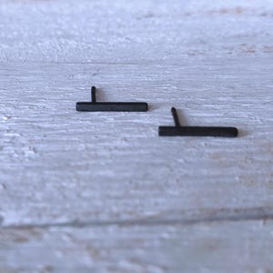 May include: A pair of black bar stud earrings. The earrings are simple and minimalist in design.