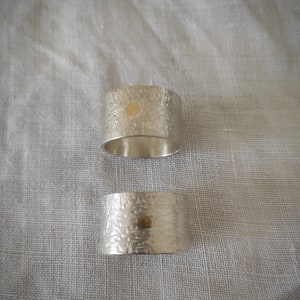 May include: Two silver rings with a textured surface and a small gold dot in the center of each ring.