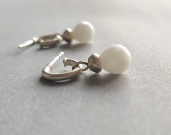 May include: A pair of silver hoop earrings with white pearl-like drops.