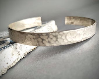May include: A silver hammered cuff bracelet with a textured surface.
