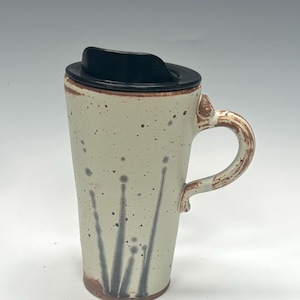 May include: A ceramic travel mug with a black lid and a handle. The mug is off-white with brown speckles and dark grey vertical designs. The handle and base have a brown, textured finish.