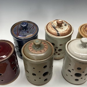 May include: Six ceramic garlic keepers with lids in various colors and patterns. The keepers have holes for air circulation.
