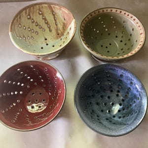 May include: Four handmade ceramic bowls with perforated designs. The bowls are in shades of green, red, blue, and brown. Each bowl has a unique color and pattern, with small holes throughout the interior.