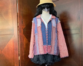 May include: A patchwork jacket in shades of red, blue, and purple, displayed on a mannequin. The jacket has a collared neckline and long sleeves. A black ruffled skirt and a straw hat complete the outfit.