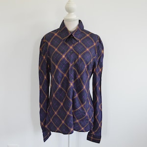 Pode incluir: Uma camisa de manga comprida com botões em azul-marinho escuro, apresentando um padrão de diamante repetido em linhas finas amarelas e roxas. A camisa tem uma gola padrão, uma carcela frontal com botões e punhos abotoados.