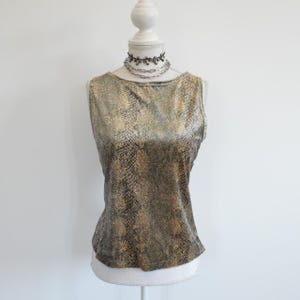 May include: A sleeveless top featuring a metallic gold and black snakeskin print pattern with a boat neckline. The garment is displayed on a white mannequin, which is also wearing a layered silver-toned chain necklace with dark accents.