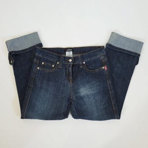 May include: Dark blue denim capri pants featuring a cuffed hem design, a front button and zipper closure, belt loops, and classic five-pocket styling. The jeans have a faded wash effect on the front panels and a Morgan brand label at the waistband.