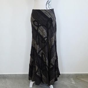 Puede incluir: Una falda larga de color gris oscuro con un patrón único. La falda presenta una combinación de rayas verticales y diagonales en tonos grises y negros. La falda se exhibe en un maniquí blanco.