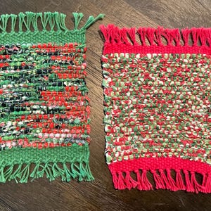 May include: Two handwoven coasters. One is green with red, black, and white accents. The other is red with green, white, and red accents. Both have fringed edges. These coasters are perfect for adding a touch of handmade charm to any home.