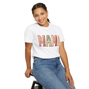 Könnte beinhalten: Ein weißes Kurzarm-T-Shirt mit dem Wort MAMA, das in großen Blockbuchstaben auf der Brust aufgedruckt ist. Jeder Buchstabe zeigt ein anderes, von Patchwork inspiriertes Muster in Rot-, Rosa-, Grün- und Cremetönen mit Blumen- und Vichy-Karomustern.