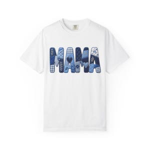 Könnte beinhalten: Ein weißes Kurzarm-T-Shirt mit dem Wort MAMA auf der Brust. Die Buchstaben sind in einem blauen Patchwork-Muster gestaltet, das verschiedene Blautöne, Vichy-Karos, florale Drucke, kleine Herzen und Knöpfe in das Design integriert.