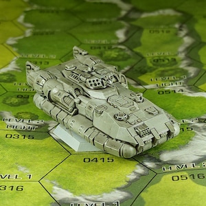 May include: A gray, detailed, futuristic-looking toy tank with a large cannon on top. The tank is sitting on a green and brown game board with numbers and text.