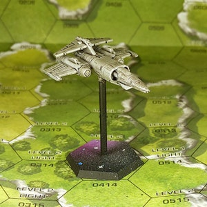 May include: A white painted miniature spaceship with a gray base. The spaceship has a long, narrow body with a pointed nose and two wings. The base is a hexagonal shape with a black and white speckled surface.