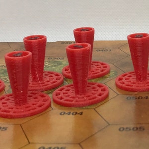 Puede incluir: Seis piezas de juego de plástico rojo con una base circular y una parte superior en forma de cono. Las piezas están dispuestas en un tablero de juego hexagonal marrón.
