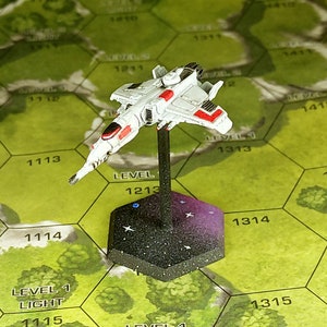 May include: A white and red spaceship miniature with a black base. The spaceship has a black cockpit and red accents. The base is a hexagonal shape with a black and white starry design.