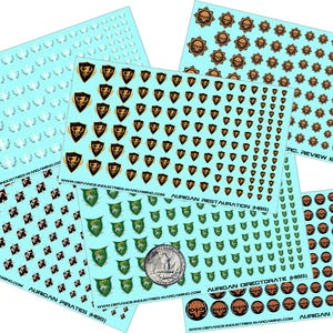 Op de afbeelding: Een verzameling decalvellen met verschillende ontwerpen, waaronder schilden, schedels en lauwerkransen, in bruin-, groen- en zilvertinten. De vellen zijn lichtblauw en bevatten tekst zoals "AURIGAN PIRATES" en "AURIGAN MERCENARIES".