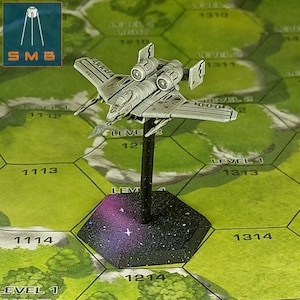May include: A grey and white miniature spaceship with two engines on the top and a black base with a galaxy design. The spaceship is on a hexagonal game board with numbers and the word "LEVEL" printed on it.