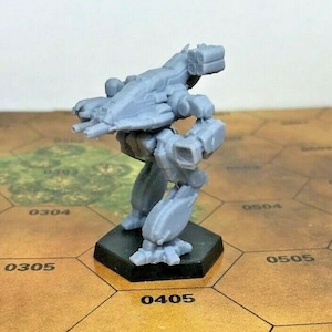 Könnte beinhalten: Eine graue Plastikminiatur eines Mech-Roboters mit einer großen Waffe auf dem Rücken. Der Roboter steht auf einem schwarzen sechseckigen Sockel. Der Sockel befindet sich auf einer braunen sechseckigen Fliese mit der Nummer 0405.