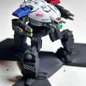 May include: A detailed model of a futuristic mech robot, primarily in white, black, and blue. The robot has multiple weapons, the text "9-1-1" and "To Protect and Serve". The robot's legs are dark gray, and the head has red and blue accents.