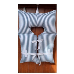 May include: A decorative life vest pillow with a blue and white striped pattern. The pillow has a unique shape with a cutout for the neck and is tied with white ribbons. The nautical-themed pillow is designed for home decor.