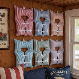 May include: Six fabric life vest wall decorations arranged in two rows of three. Each vest features vertical stripes in red, blue, or green, with white fabric ties across the front. The vests are padded and have a central cutout opening.