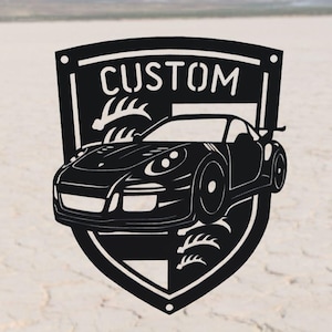 May include: Black metal wall art featuring a sports car silhouette within a shield design. The word "CUSTOM" is displayed at the top. The car has detailed features, including headlights and a spoiler. The background is a neutral, textured surface.