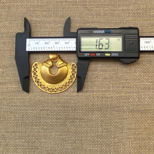 May include: A gold-colored metal pendant in the shape of a crescent moon with a circular cutout in the center. The pendant is 1.63 inches in diameter and has a detailed design with a beaded border.