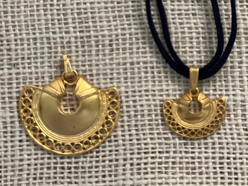 May include: Two gold pendants with intricate designs, one larger than the other, hanging on a black cord.