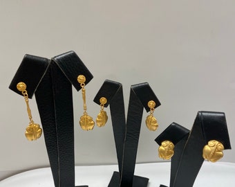 May include: Three pairs of gold-tone dangle earrings with a textured, round design. The earrings are displayed on black earring stands.