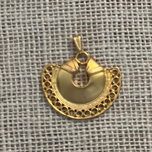 May include: A gold-colored pendant with a circular design and intricate details. The pendant is shaped like a crescent moon with a hole in the center.