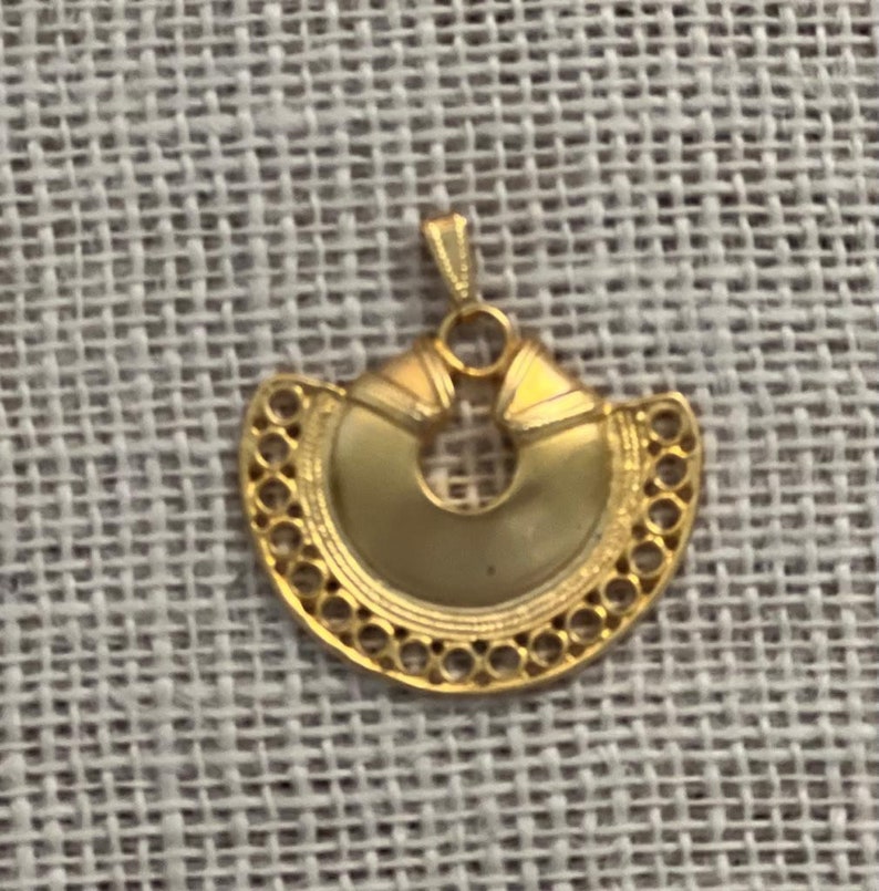 May include: A gold-colored pendant with a circular design and intricate details. The pendant is shaped like a crescent moon with a hole in the center.