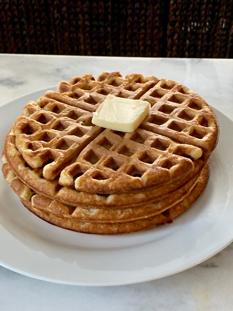 May include: A stack of three golden brown waffles with a pat of butter on top. The waffles are on a white plate.
