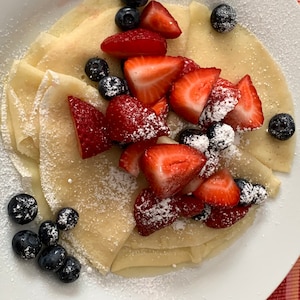 May include: A plate of thin, white crepes topped with fresh strawberries and blueberries. The crepes are dusted with powdered sugar.