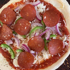May include: A pizza crust topped with tomato sauce, mozzarella cheese, pepperoni slices, red onion, and green bell pepper.