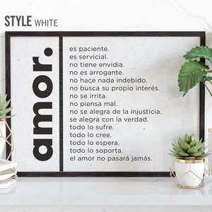 Peut inclure: Une impression encadrée noire avec un fond blanc et du texte noir. Le texte dit "amor." et énumère les qualités de l'amour en espagnol. L'impression est affichée sur une surface blanche avec deux plantes en pot.